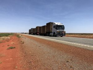 road train driving on straight stretch of highway with red dirt right next to road